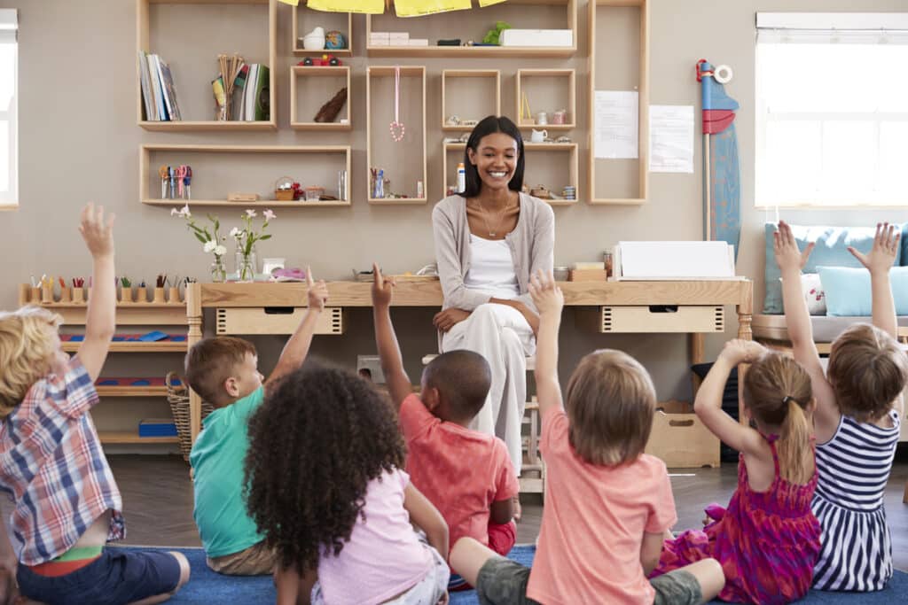 Preschool students participate in a circle time discussion, raising their hands to answer wh-questions in the classroom.